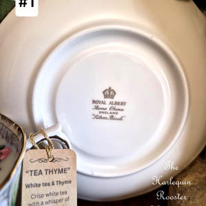 May include: A white Royal Albert Bone China saucer with the text "Silver Birch" and a tag that reads "TEA THYME" with a description of the tea. The Harlequin Rooster Hearth and Door is also visible.