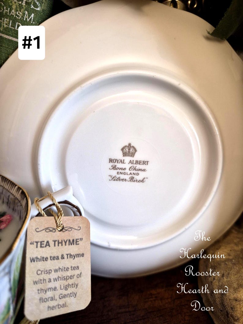 May include: A white Royal Albert Bone China saucer with the text "Silver Birch" and a tag that reads "TEA THYME" with a description of the tea. The Harlequin Rooster Hearth and Door is also visible.