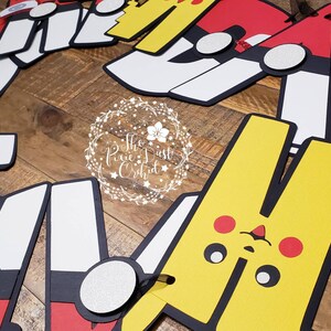 May include: A colorful paper banner with characters from the Pokemon franchise. The banner features Pikachu, Squirtle, and other Pokemon characters. The banner is perfect for a Pokemon-themed party.
