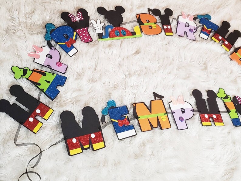 May include: A colorful felt banner with Mickey Mouse characters spelling out "Happy Birthday" and a name. The letters are decorated with glitter and different colors.