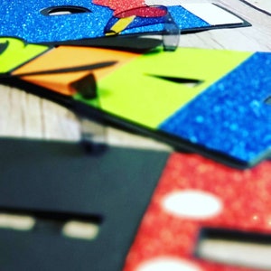 May include: Colorful letters made of foam with glitter and black trim. The letters spell out the word "HOPE".