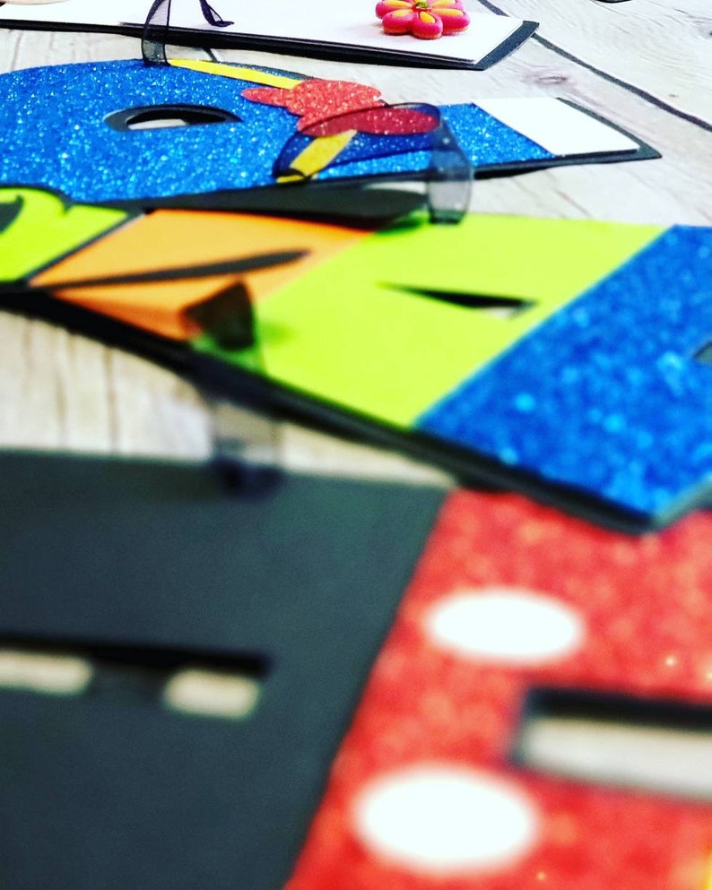 May include: Colorful letters made of foam with glitter and black trim. The letters spell out the word "HOPE".