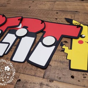 May include: A red, white, and black banner with the word "Britt" spelled out in large letters. Each letter has a Pokeball design on it. The banner also includes a yellow Pikachu character.