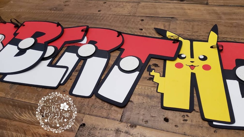 May include: A red, white, and black banner with the word "Britt" spelled out in large letters. Each letter has a Pokeball design on it. The banner also includes a yellow Pikachu character.