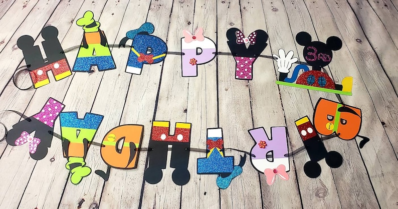 May include: A colorful Happy Birthday banner with Mickey Mouse and Minnie Mouse characters. The letters are decorated with glitter and each letter has a different character design.