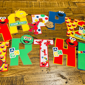 May include: A colorful Sesame Street birthday banner with letters spelling out "HAPPY BIRTHDAY". The banner features characters like Big Bird, Elmo, Cookie Monster, and Bert and Ernie.
