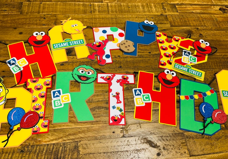 May include: A colorful Sesame Street birthday banner with letters spelling out "HAPPY BIRTHDAY". The banner features characters like Big Bird, Elmo, Cookie Monster, and Bert and Ernie.