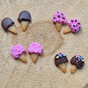May include: A selection of miniature ice cream cone charms. Some have chocolate tops, others pink, and some are decorated with sprinkles. The cones are a light brown colour.