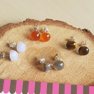 May include: A set of four pairs of earrings with different coloured stones. The earrings are displayed on a wooden surface. The stones are white, orange, brown, and grey. The earrings are handmade and are available for purchase on Etsy.
