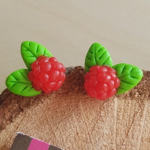 Peut inclure: Une paire de boucles d'oreilles en pâte polymère rouge et verte en forme de framboises avec des feuilles.
