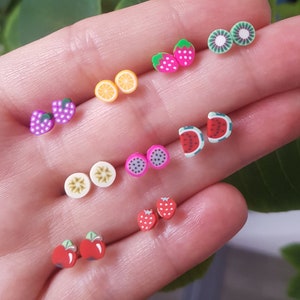 Peut inclure: Un ensemble de 10 boucles d'oreilles en forme de fruits colorés. Les boucles d'oreilles sont en pâte polymère et présentent une variété de fruits, notamment des fraises, des kiwis, des pastèques, des citrons, des fruits de la passion et des pommes.