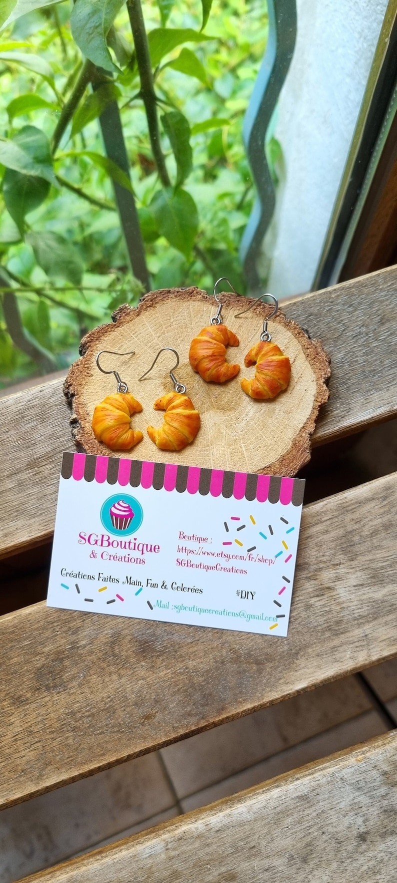 Puede incluir: Pendientes en forma de croissant hechos de arcilla polim&eacute;rica, con un glaseado dorado y marr&oacute;n. Los pendientes se muestran sobre una superficie de madera con una tarjeta de visita que dice "SGBoutique & Creations" e incluye la direcci&oacute;n del sitio web y la direcci&oacute;n de correo electr&oacute;nico. #DIY