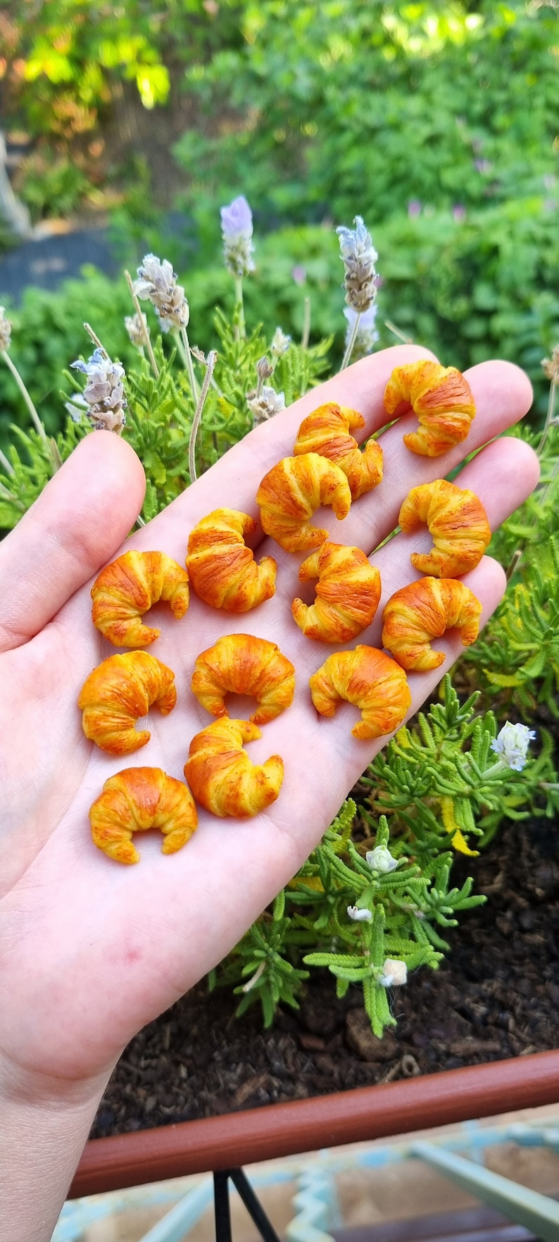 Puede incluir: Una mano sosteniendo una colecci&oacute;n de mini croissants hechos de arcilla polim&eacute;rica. Los croissants son de color amarillo claro con acentos marrones.