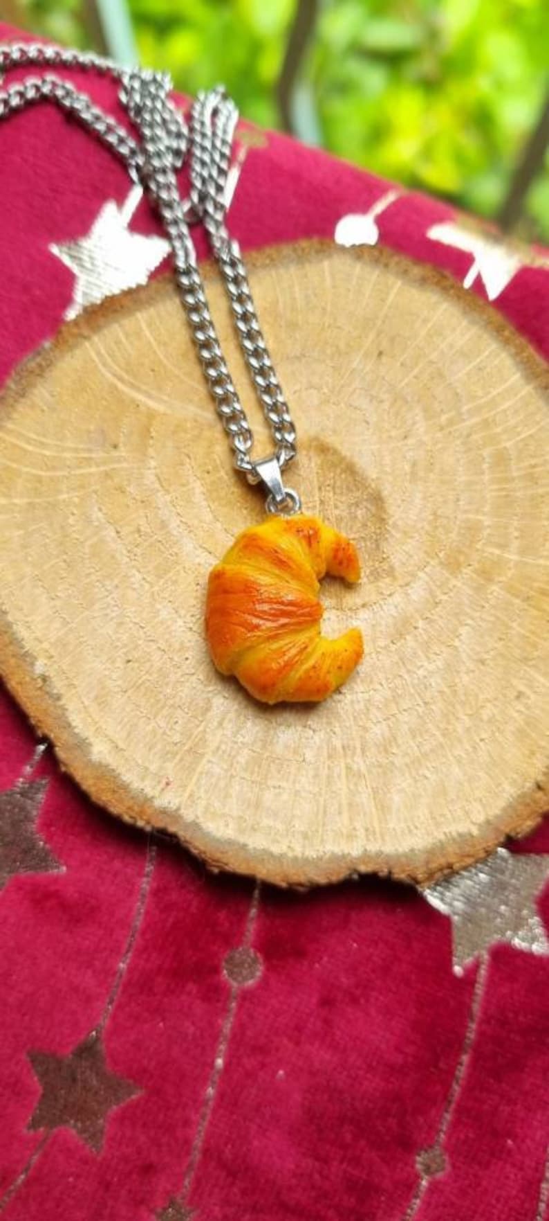 Puede incluir: Un collar de cadena plateada con un colgante de croissant. El croissant est&aacute; hecho de arcilla polim&eacute;rica amarilla y naranja y tiene forma de media luna.