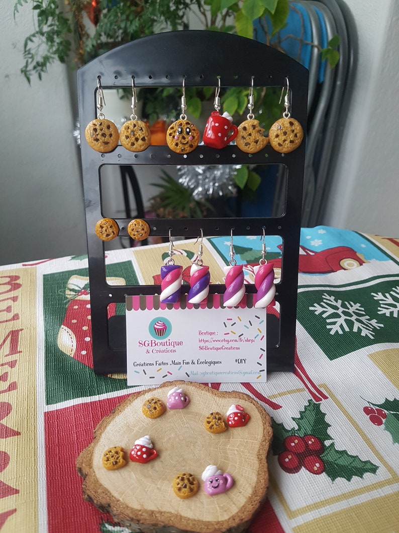 Puede incluir: Un conjunto de pendientes hechos a mano de arcilla polim&eacute;rica con varios dise&ntilde;os de comida, incluyendo galletas, tazas y bastones de caramelo. Los pendientes se muestran en un expositor de pendientes negro con una tarjeta blanca que dice "SGBoutique & Creations, Creative Fun & Eco-Elegance #DIY".