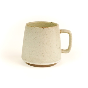 Puede incluir: Una taza de cerámica blanca con un esmalte moteado y un borde marrón. La taza tiene una base ancha y un cuerpo ligeramente cónico.