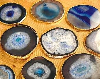 Op de afbeelding: Een verzameling agaat onderzetters met goudkleurige randen. De onderzetters hebben verschillende patronen in blauw, wit en grijs. Deze decoratieve onderzetters zijn gerangschikt op een lichtgekleurd houten oppervlak.