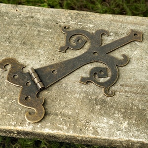 May include: A decorative brass hinge with a ornate design. The hinge is made of metal and has a dark brown finish.