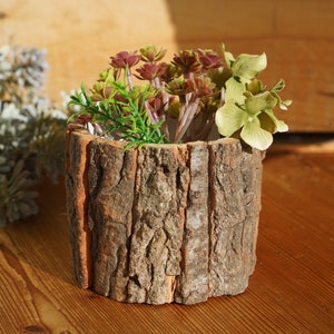 May include: A rustic wooden planter with a bark-like texture, filled with artificial succulents and green foliage.