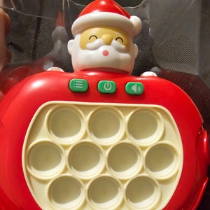 May include: A red and white Christmas themed pop it toy with a Santa Claus head on top. The toy has 12 round, white, silicone bubbles that can be pushed in and out. The toy has three buttons on the front: a speaker icon, a power button, and a button with three lines.
