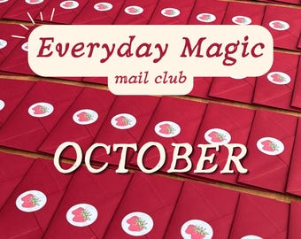 May include: A collection of deep red envelopes arranged in rows, each sealed with a circular white sticker featuring a red strawberry illustration. A central cream-colored label displays the text Everyday Magic mail club and OCTOBER.