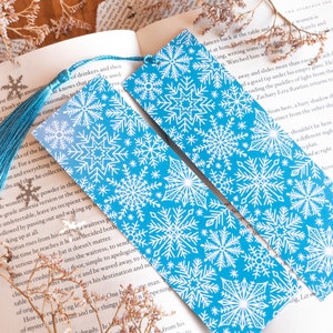 Op de afbeelding: Twee blauwe bladwijzers met sneeuwvlokkenpatroon en witte kwastjes. De bladwijzers liggen op een boek met tekst over een man genaamd Zachary Erra Rawlins.