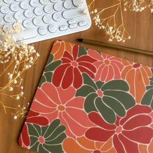 May include: A colorful desk mat with a floral pattern in shades of red, orange, green, and pink. The mat features large, stylized flowers with rounded petals.