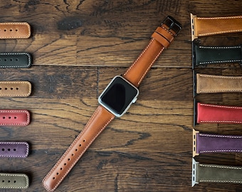 Puede incluir: Una correa de Apple Watch de cuero marrón con una esfera plateada. La correa se muestra con una variedad de otras correas de reloj en diferentes colores y materiales.