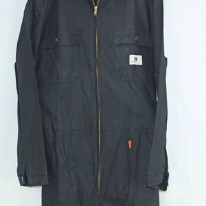 May include: Black workwear jumpsuit with a zipper closure and two chest pockets. The jumpsuit has a small yellow and black logo patch on the chest that says "IS Workwear".