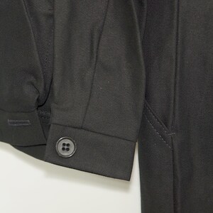 May include: A black long-sleeved jacket with a button on the cuff. The jacket has a seam down the side and a pocket on the right side.