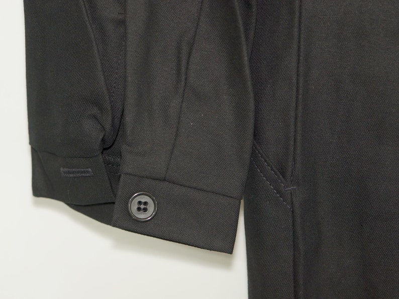May include: A black long-sleeved jacket with a button on the cuff. The jacket has a seam down the side and a pocket on the right side.