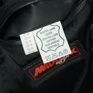 May include: A black leather jacket with a white label that reads "Echtes Lamm Leder, Genuine Lamb Leather, Cuir Agneau Veritable". The label also has a care symbol and a "P" symbol. The jacket has a zippered pocket and a red label that reads "Mad" with a stylized bird logo.