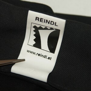 May include: White label with black text and a logo. The text reads "REINDL" and "www.reindl.at". The logo is a stylized black and white image of a mountain.