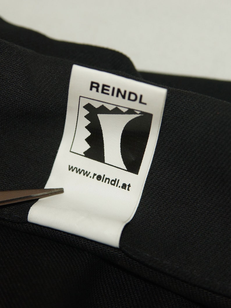 May include: White label with black text and a logo. The text reads "REINDL" and "www.reindl.at". The logo is a stylized black and white image of a mountain.
