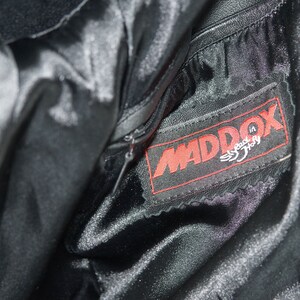 May include: Close-up of a black leather jacket with a zipper and a red label that says "MADDOX Speed in Italy".