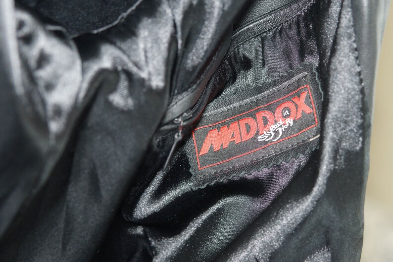 May include: Close-up of a black leather jacket with a zipper and a red label that says "MADDOX Speed in Italy".