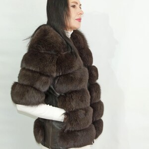 May include: A brown fur jacket with a leather trim and a zipper closure. The jacket has a stand-up collar and is made of multiple layers of fur.