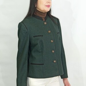 Könnte beinhalten: Ein grüner Blazer mit schwarzem Muster, einem Stehkragen und fünf goldenen Knöpfen. Der Blazer hat einen schwarzen Besatz an Kragen, Taschen und Saum.