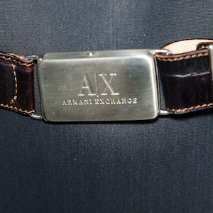 May include: A brown leather belt with a silver buckle that says "AX ARMANI EXCHANGE".
