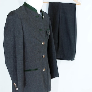 May include: A dark gray suit jacket and matching trousers. The jacket features gold buttons, dark green trim, and a mandarin collar. The trousers are hanging on a wooden hanger.