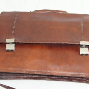 May include: A brown leather briefcase with a silver clasp and a shoulder strap.