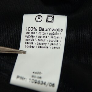 May include: White tag with black text indicating the fabric content is 100% cotton. The tag lists the word "Baumwolle" in German, and the word "cotton" in English, French, Spanish, Italian, and Portuguese. The tag also lists the word "cotton" in several other languages.