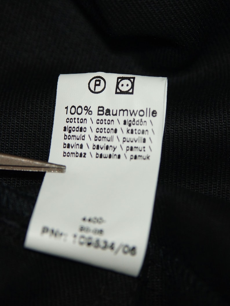 May include: White tag with black text indicating the fabric content is 100% cotton. The tag lists the word "Baumwolle" in German, and the word "cotton" in English, French, Spanish, Italian, and Portuguese. The tag also lists the word "cotton" in several other languages.