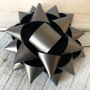 May include: A metallic silver bow with a starburst design. The bow has a layered construction with pointed tips and a dark interior. This decorative bow is suitable for gift wrapping or craft projects.