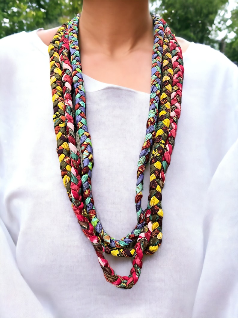 Op de afbeelding: Een veelkleurige gevlochten ketting gemaakt van stofresten. De ketting is gelaagd en heeft tinten rood, groen, geel, blauw en bruin.