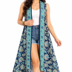 May include: A sleeveless, open-front duster vest featuring a dark blue base with a multi-colored floral and paisley print. The garment has a high-low hemline and a contrasting light blue and tan vertical border along the front opening.