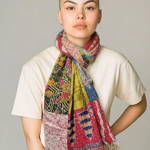 May include: A colorful patchwork scarf with a variety of patterns and colors, including red, green, blue, and yellow. The scarf is made of a soft fabric and has a fringed edge. The scarf is wrapped around the neck.
