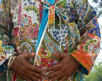 Può includere: Una giacca colorata in patchwork con una fascia blu annodata in vita. La giacca ha un motivo paisley ed è realizzata in cotone.