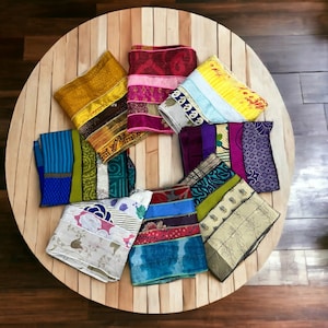May include: A collection of 10 colorful fabric squares arranged in a circle on a wooden table. The squares are made of different fabrics and patterns, including floral, geometric, and striped designs. The colors include yellow, blue, green, purple, pink, and white.