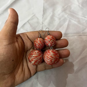 May include: A pair of red and gold thread earrings with a dangling ball design.